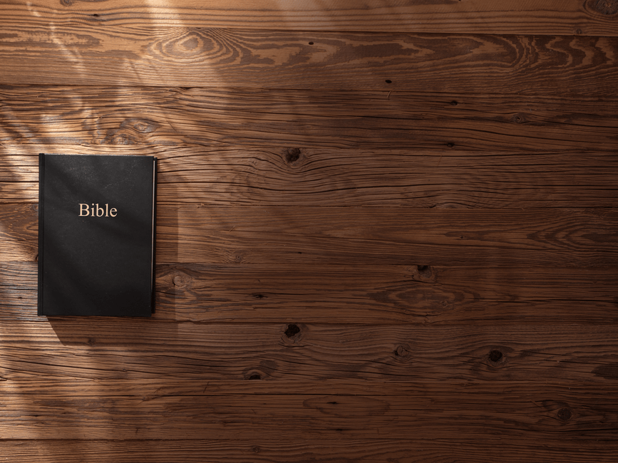 Bible resting on a wooden surface with soft shadows creating a serene atmosphere.