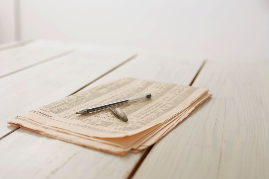 Elegant close-up of a newspaper with a pen on a wooden table, highlighting simplicity and calm.