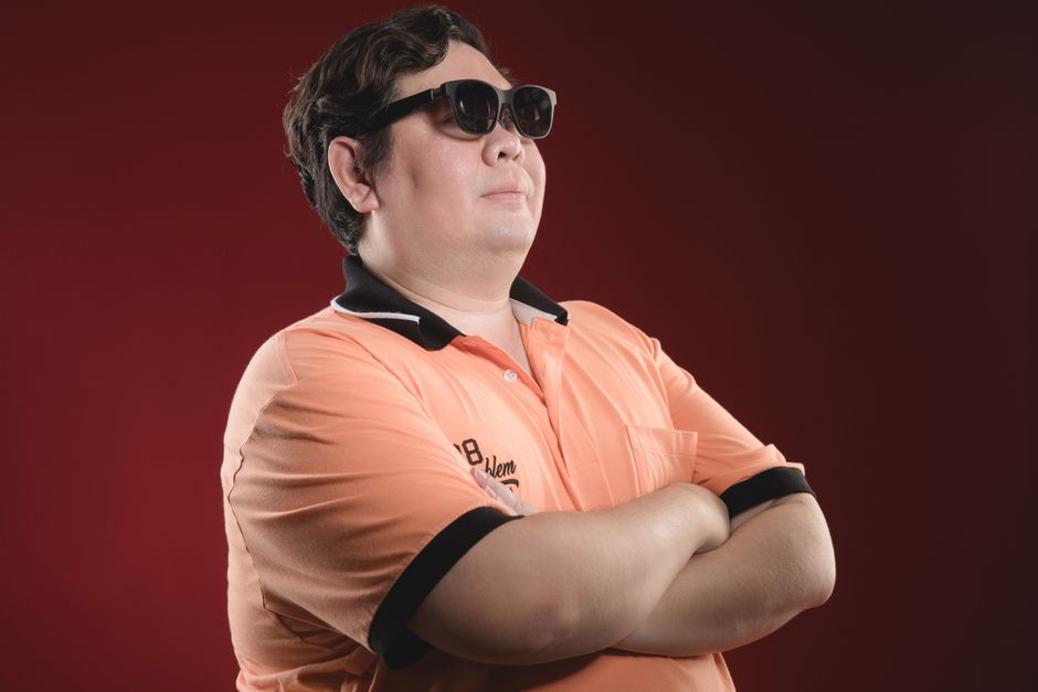 Portrait of a confident Asian man in a polo shirt and sunglasses against a red background.